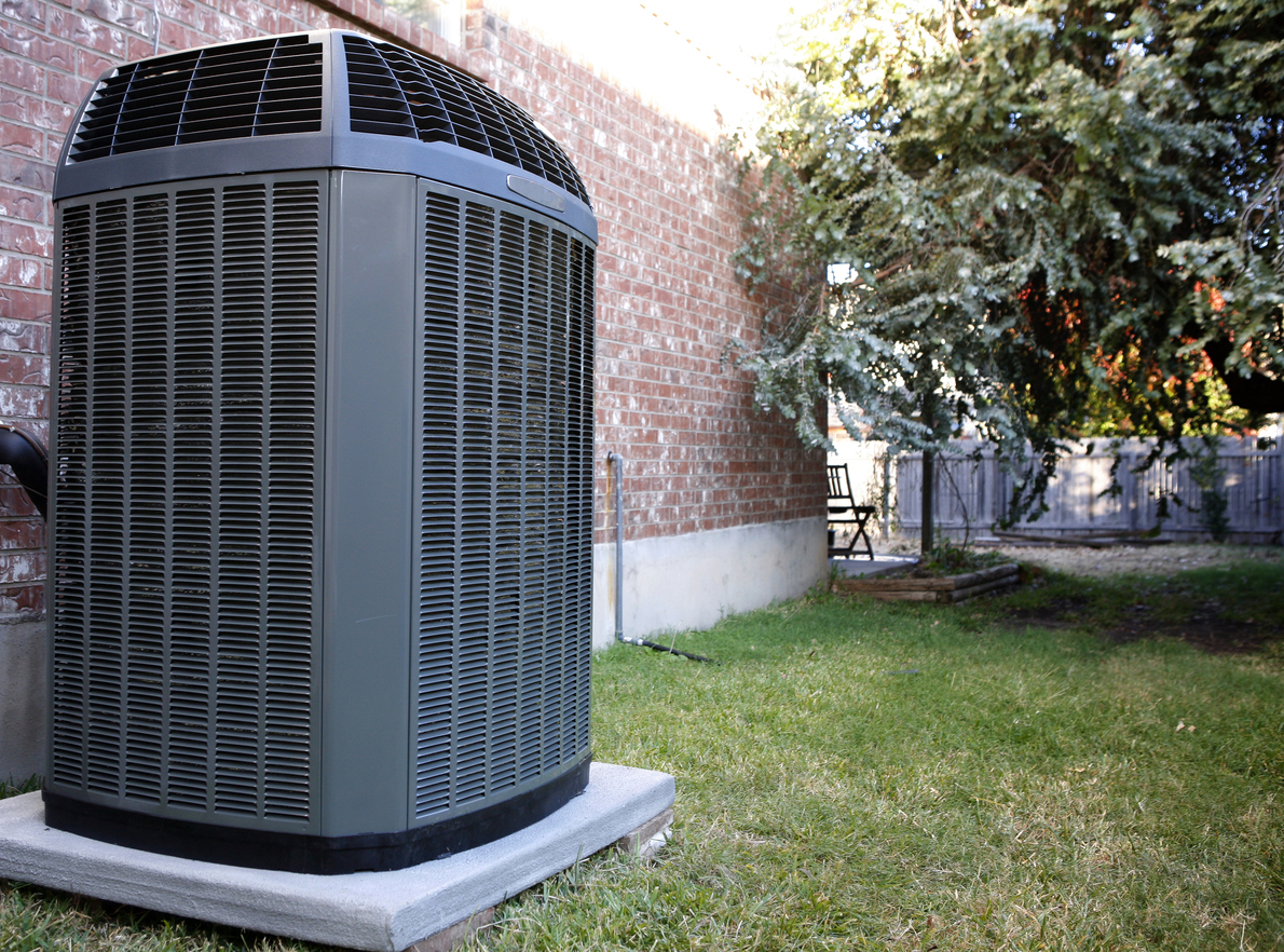 Air conditioning unit installed outdoors against home's brink wall