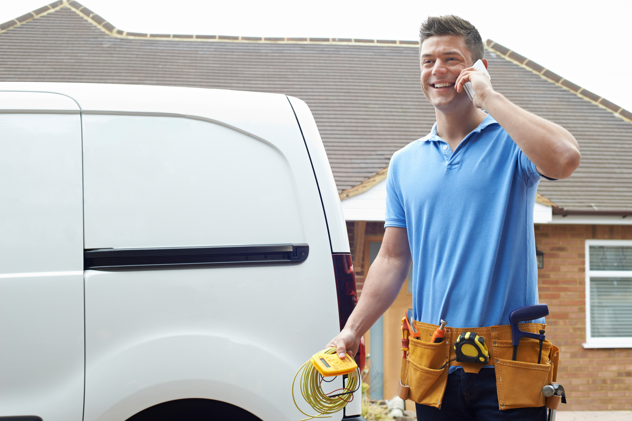 HVAC technician standing in front of a white work van while talking on the phone