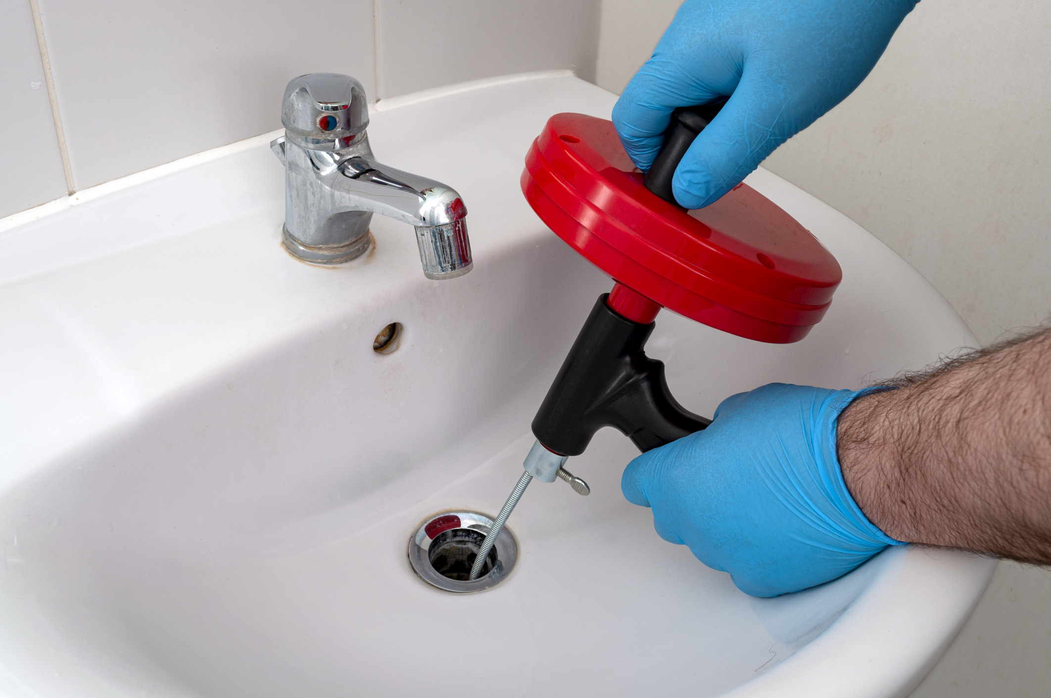 Man’s hands using a drain snake to clean a sink drain